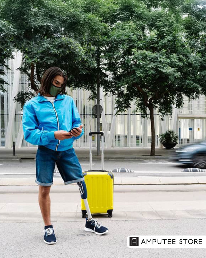 Amputee traveler with a prosthetic leg standing beside a yellow suitcase while checking their phone, representing independence and practical tips for solo travel with a prosthetic.