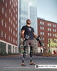 Brian Douglas, a bilateral lower limb amputee, stands outside a university building wearing prosthetic legs and holding another pair of prostheses in both hands.