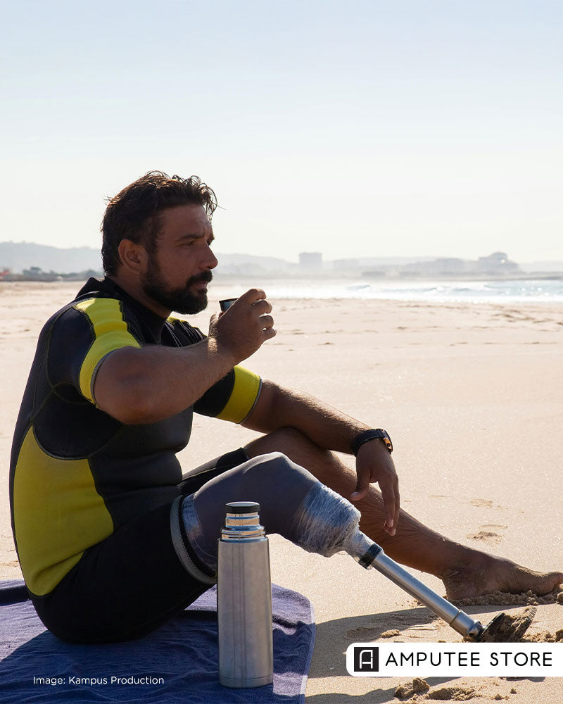 A man with a prosthetic leg is sitting on a beach, drinking from a cup, promoting tips to create a daily routine for amputees.