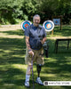 Bob Aims, a below-knee amputee, holds a compound bow at an outdoor archery range, highlighting the benefits of adaptive archery and peer support after limb loss.