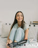 A smiling young woman with a prosthetic arm sits on a bed, representing amputees looking for funding options and resources to afford prosthetic limbs in the U.S., UK, and Europe. 