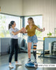 Young woman with a below-knee prosthetic leg practicing balance on a stability trainer with guidance from a physical therapist in a modern rehab clinic. 