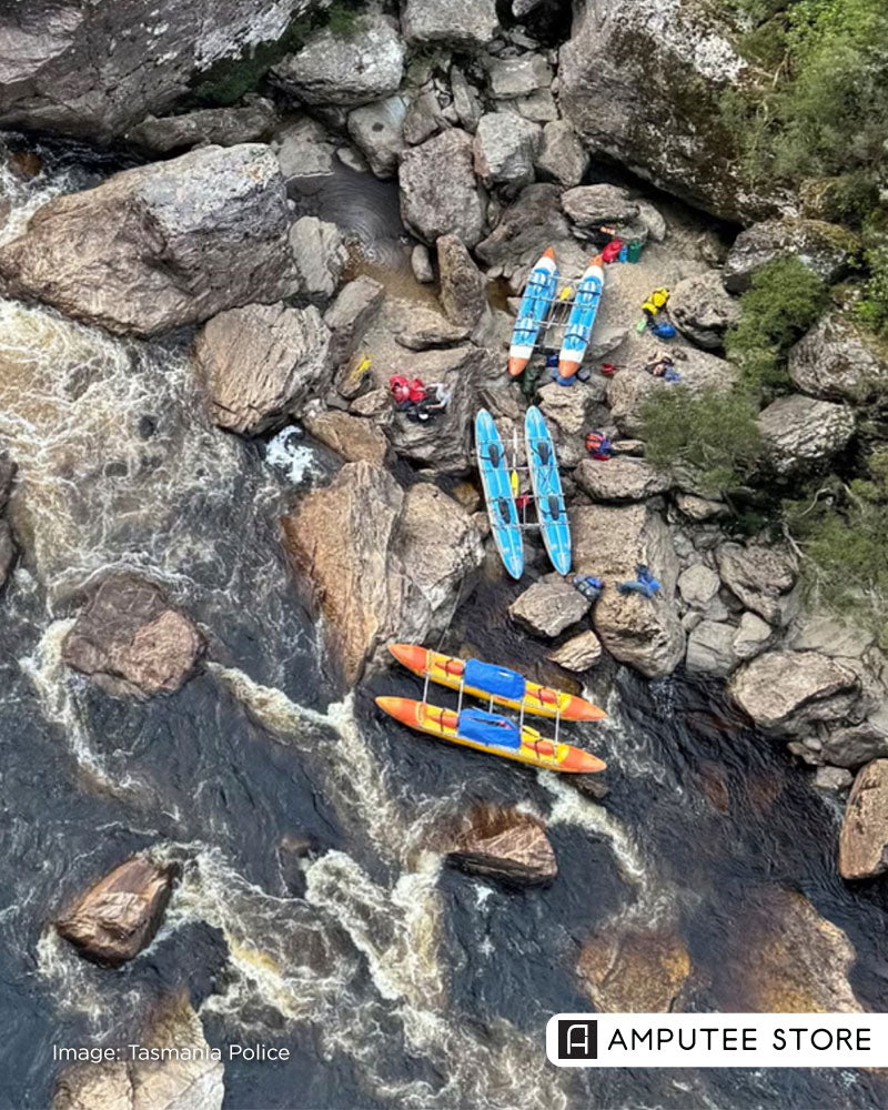 An aerial view of a rocky riverbank with rafts and rescue personnel gathered near turbulent rapids. 