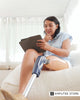 A woman with a prosthetic leg is relaxing on a couch while using a tablet, promoting self-care tips and mental health support for amputees waiting for professional help.