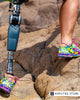 Person wearing the Lindhe Xtend Foot Först prosthetic foot navigates rocky terrain in colorful athletic shoes.
